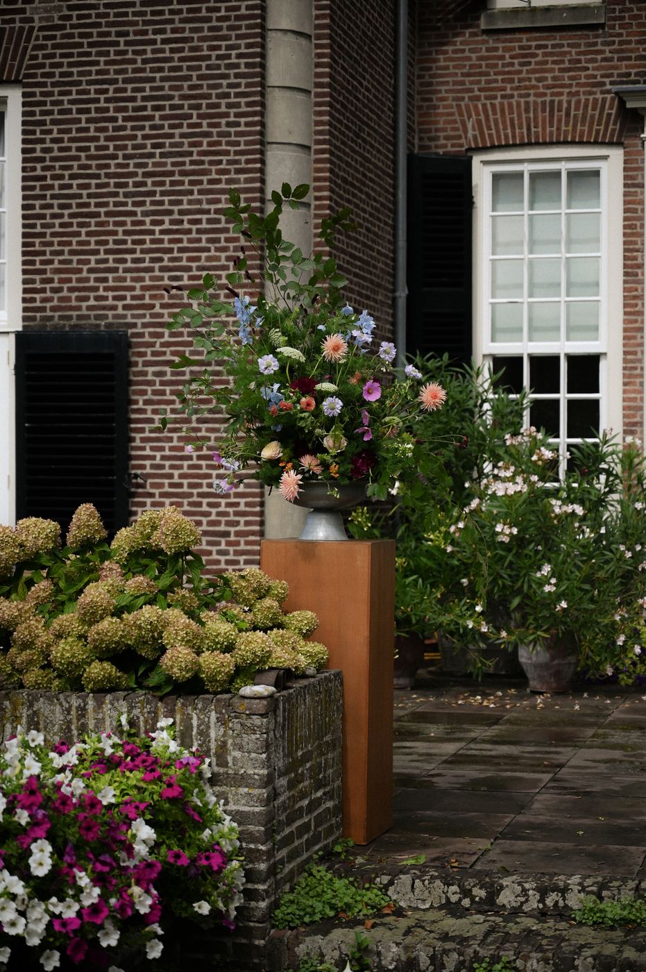 Bloemsculptuur op een cortenstalen sokkel voor een bakstenen gevel