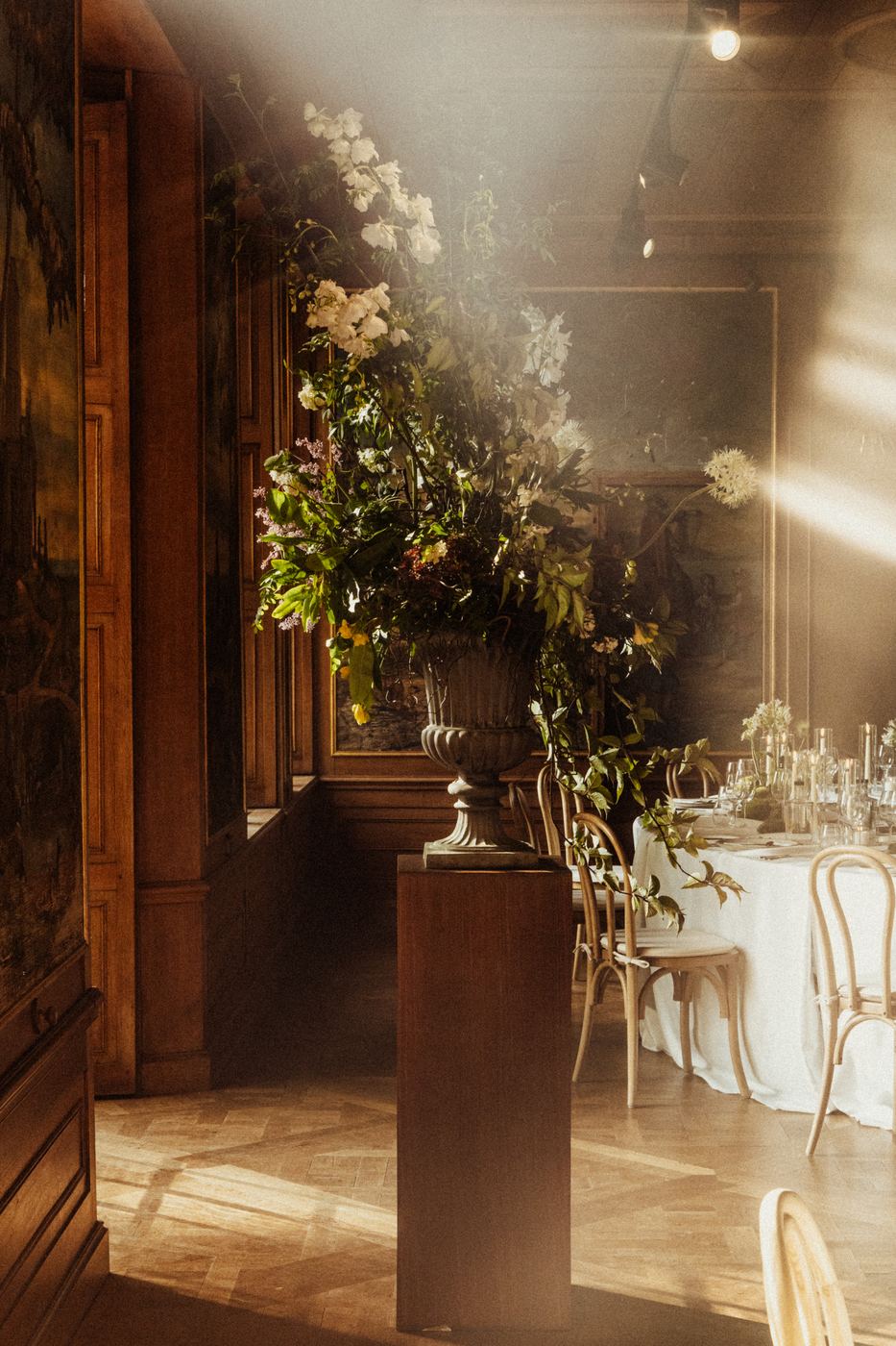 Urn met bloemen bij een gedekte dinertafel in invallend licht